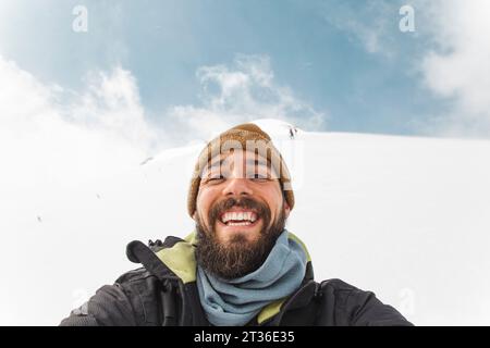 Homme heureux portant un chapeau en tricot prenant selfie dans la neige Banque D'Images