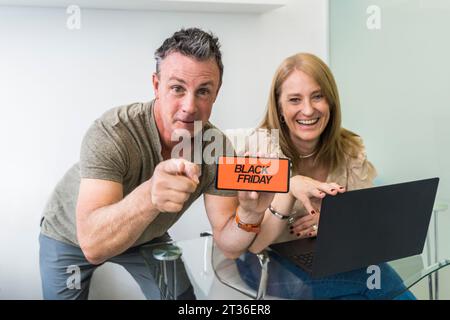 Un homme tient un téléphone portable avec une publicité Black Friday à l'écran avec sa femme de son côté. Banque D'Images