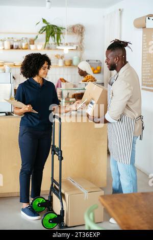 Serveur souriant tenant le paquet et femme de livraison scannant le code QR dans le café Banque D'Images