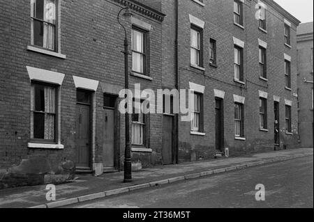 Dame regardant de sa porte dans une rue de maisons mitoyennes victoriennes, pendant le nettoyage des bidonvilles et la démolition de St ann's Nottingham, 1969-1972 Banque D'Images