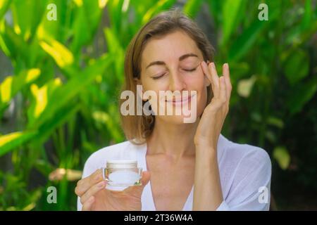 Gros plan du visage d'une belle femme d'âge moyen. Une femme applique de la crème. Banque D'Images