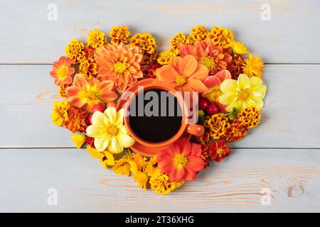 Composition d'automne d'une tasse de café rouge et dahlia, fleurs de souci en forme de coeur sur fond de bois bleu avec une place pour le texte. Pose à plat Banque D'Images