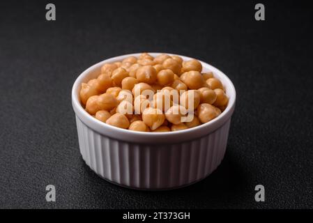 Délicieux pois chiches en conserve dans une assiette en céramique sur un fond de béton foncé. Ingrédient pour plats végétariens Banque D'Images