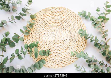 Tapis de place en osier avec des branches d'eucalyptus sur une table. Maquette pour cosmétiques. Soins de la peau, concept de traitement de beauté. Vue de dessus, pose à plat. Banque D'Images