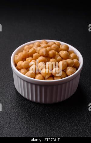 Délicieux pois chiches en conserve dans une assiette en céramique sur un fond de béton foncé. Ingrédient pour plats végétariens Banque D'Images