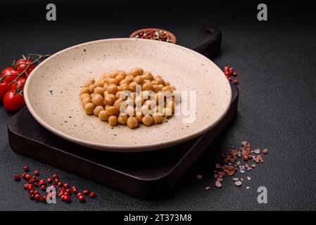 Délicieux pois chiches en conserve dans une assiette en céramique sur un fond de béton foncé. Ingrédient pour plats végétariens Banque D'Images