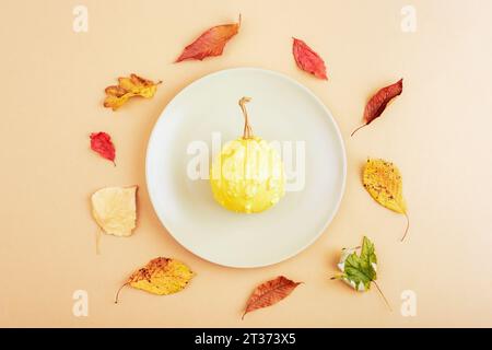 Place de table d'automne avec assiette grise avec citrouille et feuilles jaunes sur fond neutre. Thanksgiving, décoration d'halloween. Vue de dessus, plat la Banque D'Images