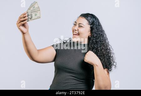 Jeune femme victorieuse détenant de l'argent célébrant isolé. Fille latine excitée détenant de l'argent liquide isolé Banque D'Images
