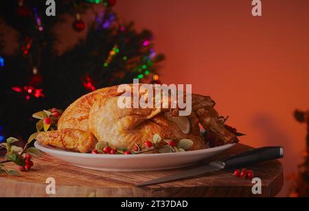 dinde rôtie de Noël, poulet reposant sur une assiette à la table à manger avec un arbre de Noël en arrière-plan Banque D'Images