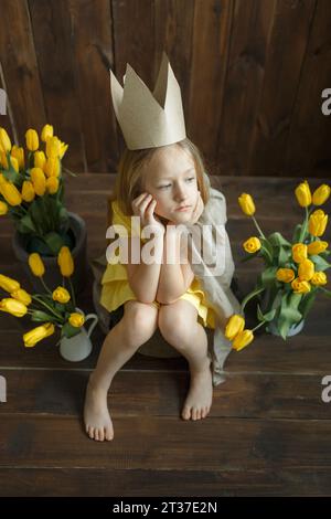 Portrait d'une princesse triste assis à côté de bouquets de tulipes jaunes.elle est assise triste, pensant. Cadre vertical. Banque D'Images