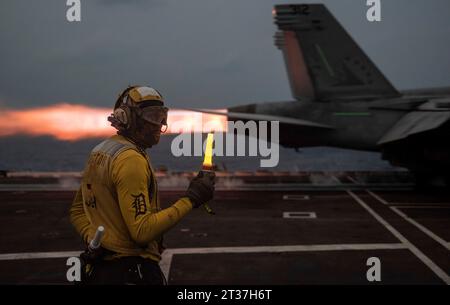 USS Ronald Reagan, Japon. 17 octobre 2023. Le directeur de vol de l'US Navy ABH3 Julian Bibb, regarde un avion de chasse F/A-18E Super Hornet, attaché à l'Eagles of Strike Fighter Squadron 115, déclenche les postbrûleurs pour lancer au crépuscule du poste d'envol du super-porteur nucléaire de classe Nimitz, USS Ronald Reagan lors d'opérations nocturnes en mer de Chine orientale, le 17 octobre 2023 au large des côtes du Japon. Crédit : MC3 Jordan Brown/US Navy photo/Alamy Live News Banque D'Images