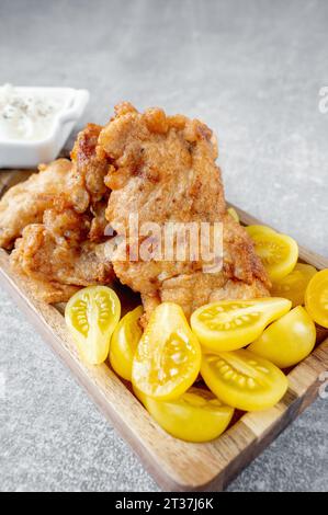 Le plat de poisson est du filet de morue frit avec une sauce crémeuse et des tomates prunes jaunes, servi sur un plateau en bois en forme de poisson. Espace de copie Banque D'Images