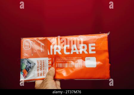 Paris, France - 1 septembre 2023 : main masculine tenant une pochette à bagages Happy Flight pour le soin des cheveux, fabriquée par Alife Design, sur fond rouge défocalisé. Banque D'Images