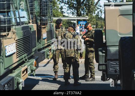 16.08.2023 Varsovie, Pologne. Trois soldats sérieux se tenant entre des camions militaires modernes se préparant pour un événement militaire en plein air. Photo de haute qualité Banque D'Images