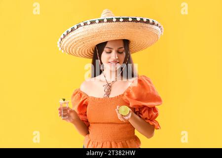 Belle jeune femme mexicaine en sombrero et avec tequila sur fond jaune Banque D'Images