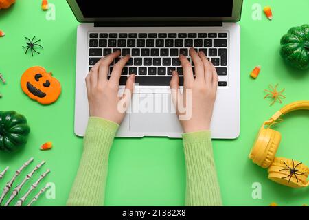 Mains féminines avec ordinateur portable, écouteurs et décorations d'Halloween sur fond vert Banque D'Images