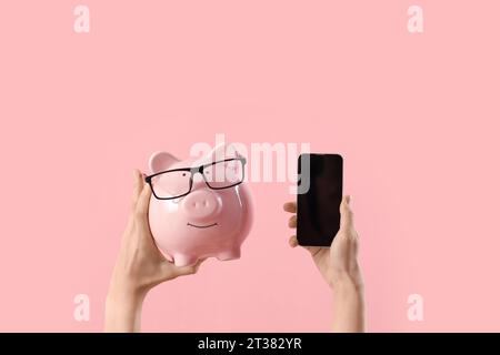 Femme avec tirelire et téléphone portable vierge sur fond rose Banque D'Images
