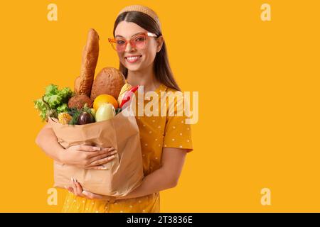 Jeune femme tenant un sac en papier avec des légumes frais sur fond jaune Banque D'Images