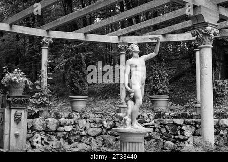 Codman Farm - Lincoln, Massachusetts 2023 - Une statue classique en pierres blanches sur un homme grec et un enfant sur un pilier en dessous d'un grand treillis de raisin avec fougère Banque D'Images