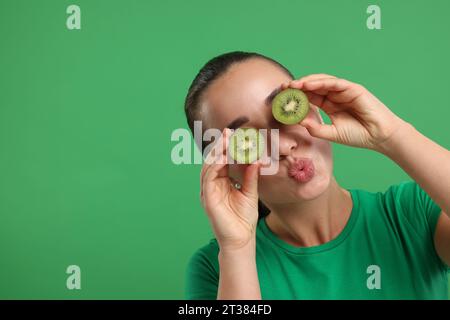 Femme couvrant les yeux avec des moitiés de kiwi sur fond vert, espace pour le texte Banque D'Images