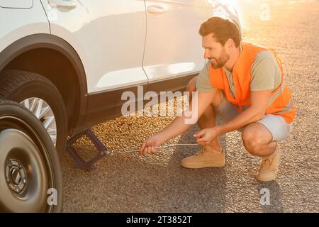 Homme changeant la roue de la voiture sur le bord de la route Banque D'Images