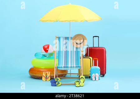 Chaise longue, parasol, valises et accessoires de plage sur fond bleu clair. Vacances d'été Banque D'Images