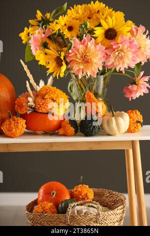 Composition d'automne avec de belles fleurs et citrouilles sur la table de console près du mur gris foncé Banque D'Images