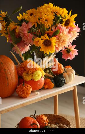 Composition d'automne avec de belles fleurs et citrouilles sur la table de console près du mur gris foncé Banque D'Images