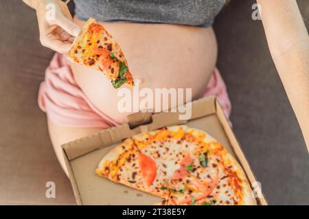 Une femme enceinte apprécie une tranche de pizza, savourant un moment de plaisir tout en satisfaisant son envie d'un régal délicieux et réconfortant. Excité Banque D'Images