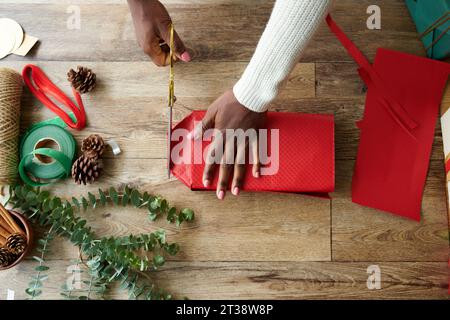 Mains de la personne enveloppant des boîtes-cadeaux dans du papier rouge, vue de dessus Banque D'Images