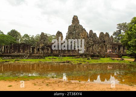 Une photo du temple de Bayon prise de l'entrée nord. Les sculptures de visages sereins sont visibles sur les tours de grès et une statue assise peut l'être Banque D'Images