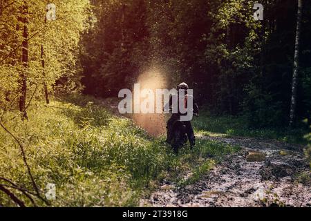 moto coureur sur enduro sports moto roule sur une route boueuse avec des flaques d'eau avec des éclaboussures dans la forêt dans une course hors route sur une journée ensoleillée Banque D'Images