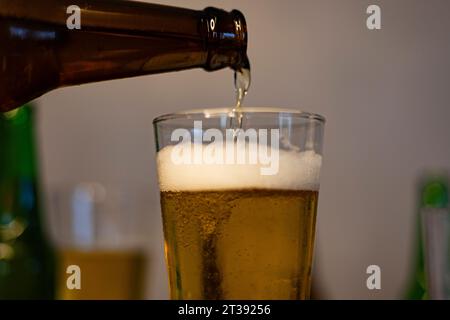 Gros plan. Verser la bière dans le verre. La bière est versée de la bouteille brun foncé dans le verre à bière. Banque D'Images