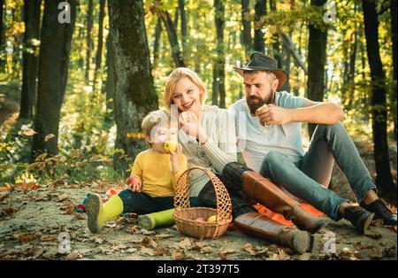 Pique-nique familial au parc forestier. Il y a un panier avec repas et jouets pour l'enfant. Le concept d'une famille heureuse. Maman, papa et bébé heureux assis à Banque D'Images