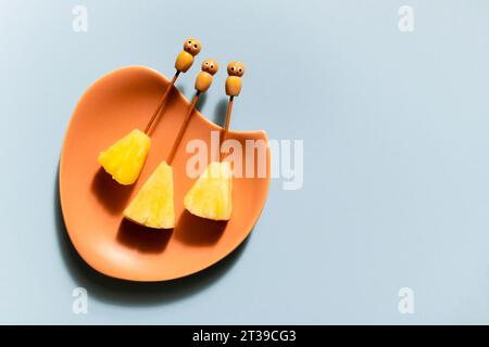 Trois tranches d'ananas frais avec des bâtons de cocktail drôles présentés sur une assiette vintage. Banque D'Images