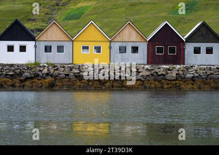 Groupe de petites maisons multicolores situées ensemble sur la côte pierreuse d'un lac calme dans une nature herbeuse sur les îles Féroé Banque D'Images