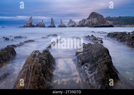 Longue exposition des vagues se jetant sur les rochers et les falaises contre le ciel nuageux dans les Asturies, Espagne Banque D'Images