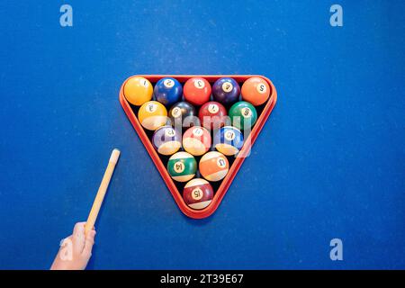 Vue de dessus de la pyramide colorée de boules de billard dans le triangle de billard placé sur la table de billard bleue près de la personne anonyme de récolte avec repère Banque D'Images