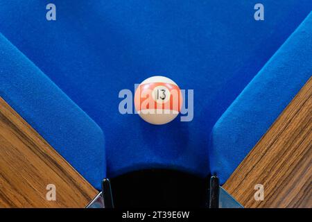 Vue de dessus de la boule de billard orange et blanc sur la table de billard bleue près de la poche Banque D'Images