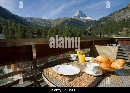 Une salle à manger en plein air donnant sur la majestueuse montagne Matterhorn, avec une variété de plats pour le petit-déjeuner, notamment du jus d'orange, des croissants et du café Banque D'Images