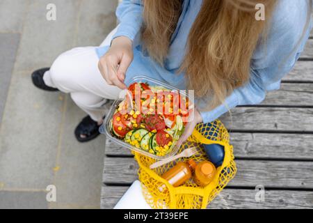 Anonyme jeune femme caucasienne avec de longs cheveux blonds, portant une chemise bleue et un pantalon blanc, profitant d'un vibrant avec tomate, maïs, poivre, laitue et Banque D'Images