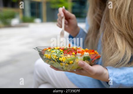 Gros plan d'une jeune étudiante blonde caucasienne méconnaissable aux cheveux blonds, tenant une fourchette et savourant une salade fraîche à l'heure du déjeuner. Banque D'Images
