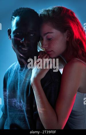 Portrait d'un couple d'amour multiracial qui s'embrassent intimement une ambiance disco avec fond bleu Banque D'Images