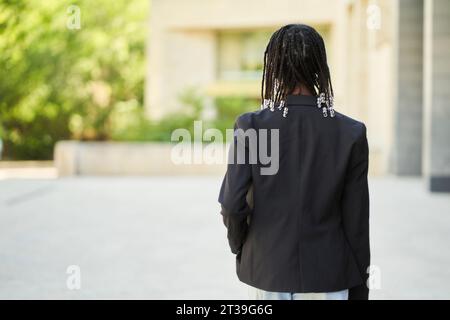 Vue arrière d'une femme d'affaires afro-américaine méconnaissable avec des tresses afro portant une tenue élégante marchant contre le bâtiment Banque D'Images