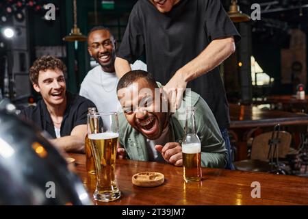 homme touchant les épaules du marié afro-américain excité pendant la fête de célibataire, amitié masculine Banque D'Images