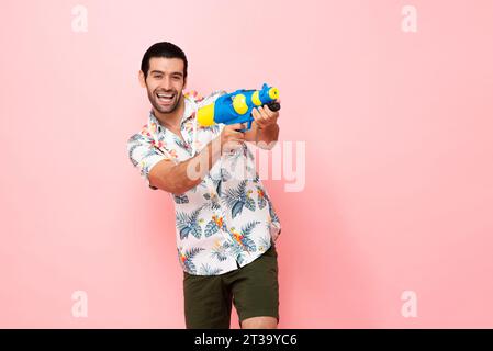 Joyeux souriant jeune homme touristique caucasien jouant avec un pistolet à eau dans le fond rose studio pour le concept de festival Songkran en Thaïlande et au sud-est Banque D'Images