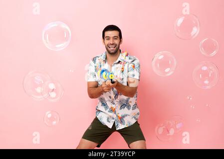 Beau souriant jeune homme touristique caucasien jouant avec un pistolet à eau dans le fond rose studio pour le concept de festival Songkran en Thaïlande et au sud-est Banque D'Images