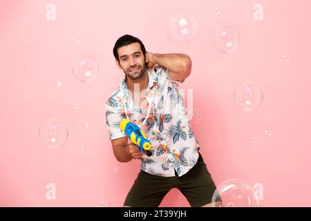 Beau souriant jeune homme touristique caucasien jouant avec un pistolet à eau dans le fond rose studio pour le concept de festival Songkran en Thaïlande et au sud-est Banque D'Images