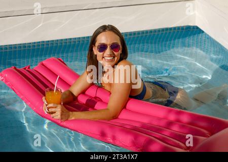 Sérénité estivale : Femme élégante se détendant sur Pink Float dans la piscine Banque D'Images