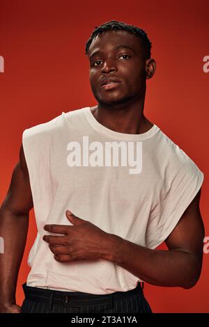 homme afro-américain élégant charismatique dans un débardeur blanc regardant la caméra sur le rouge, style moderne Banque D'Images